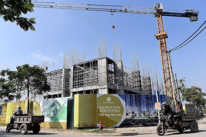 This photograph on 4 December 2020 shows workers carrying goods past a building still under construction in Hanoi. Picture: Nhac NGUYEN / AFP.